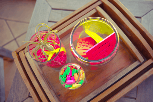 Overhead shot of neon details from a party that include an air plant, erasers and calculators.