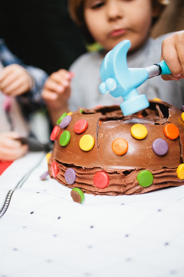A kid using a toy hammer to break the hard chocolate shell of a birthday cake. 