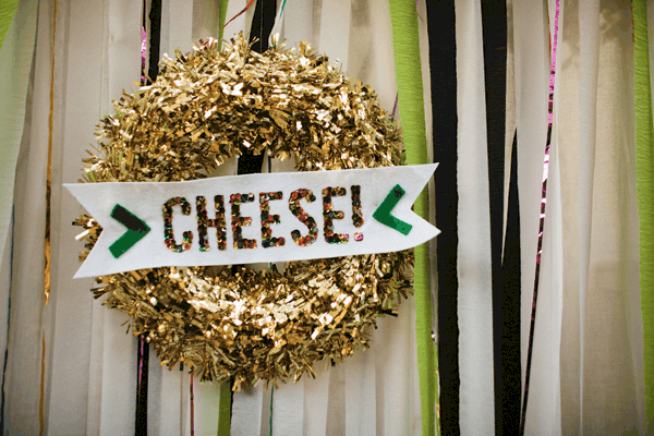 Gold wreath with the word "cheese" on the party booth backdrop from a party.