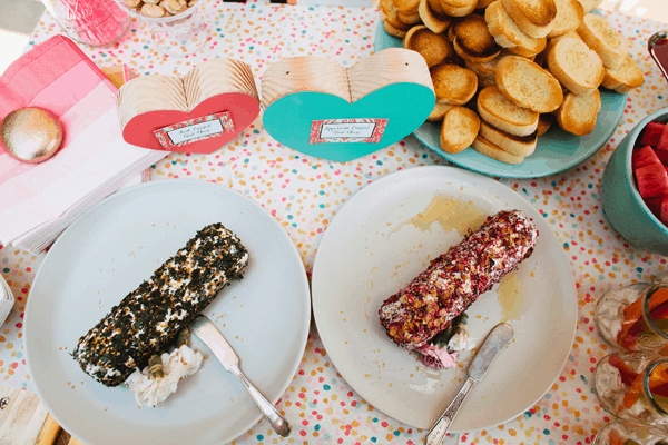 Two goat cheese log appetizers on a table next to wooden heart decoration.