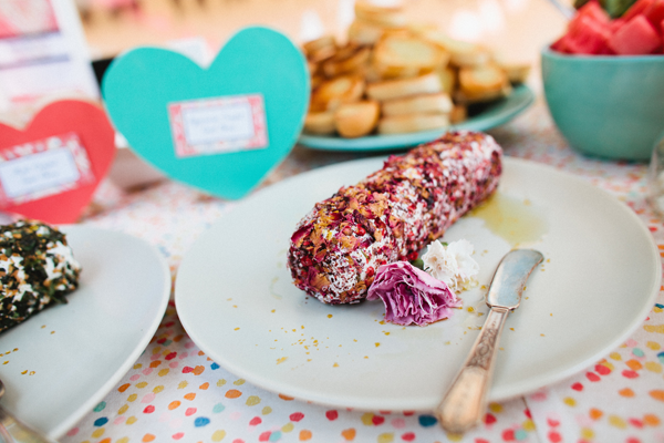 Goat cheese log, rolled in rose petals and sumac on a plate with a cheese knife.