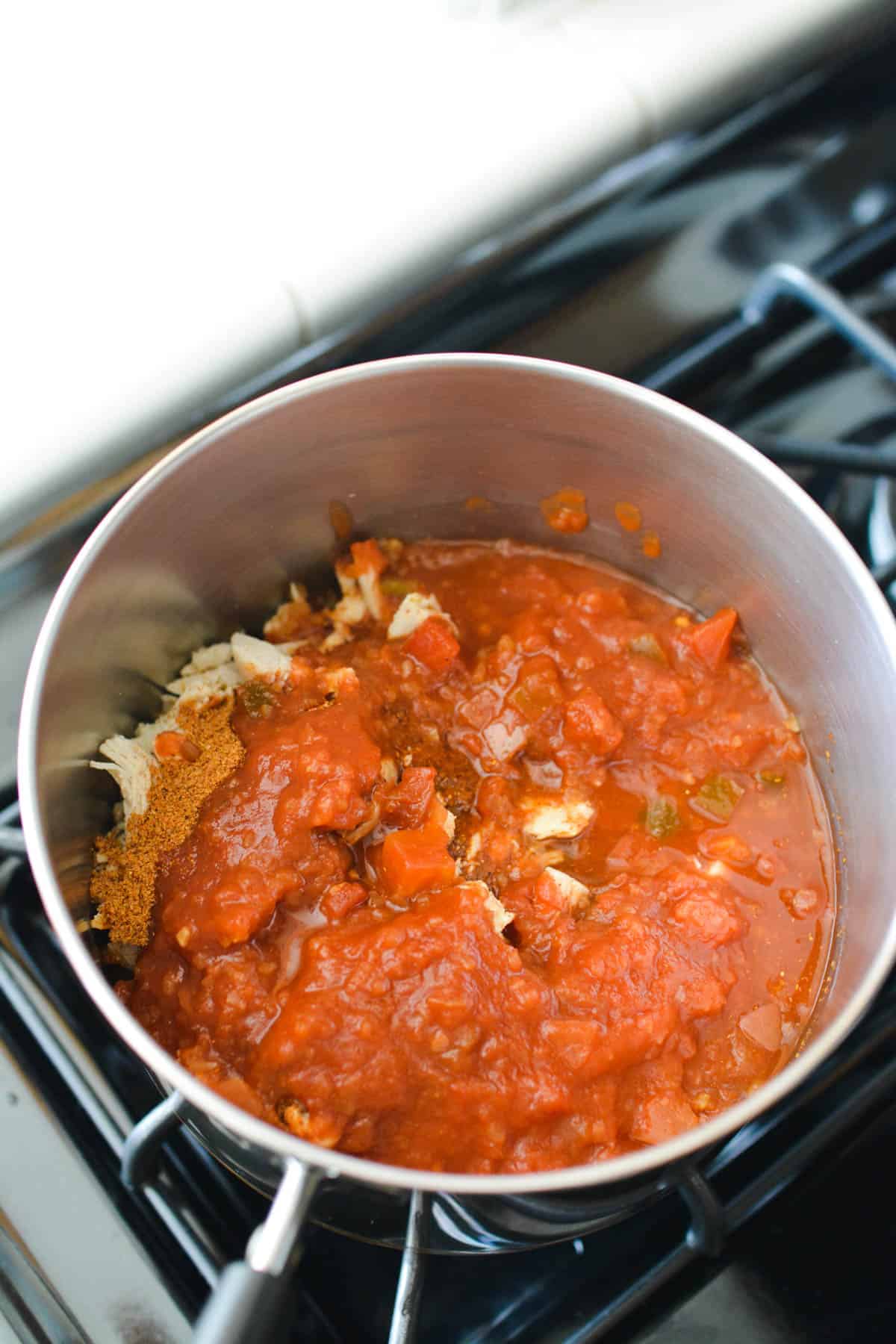 A pan on the stove with shredded chicken and salsa.