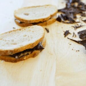 Two chocolate sandwiches next two chopped dark chocolate on a wooden cutting board.