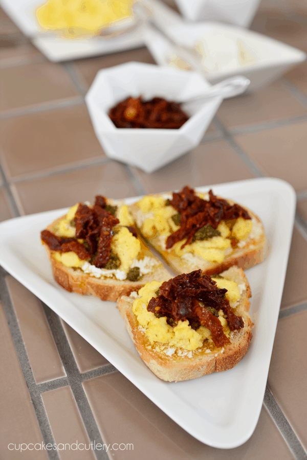 A triangle plate with toast pieces topped with goat cheese, scrambled eggs and sun-dried tomatoes for brunch.