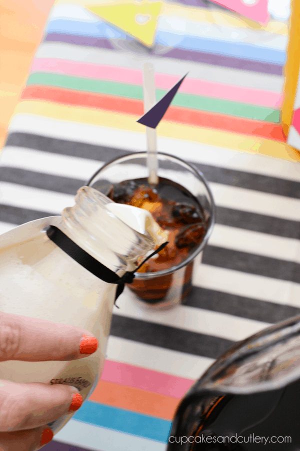 Pouring creamers into a glass of iced coffee.