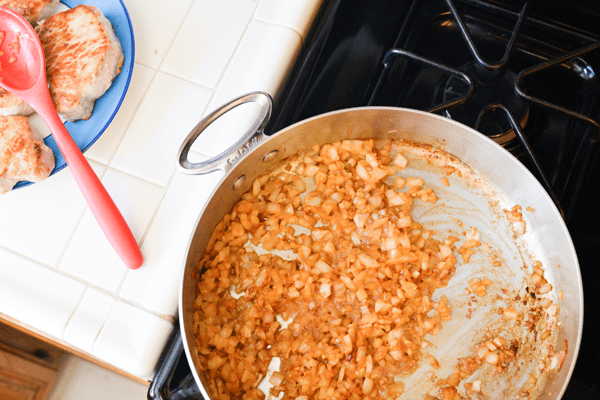 An overhead view of cooked onions in a frying pan with pork chops on a plate on the counter next to it. 