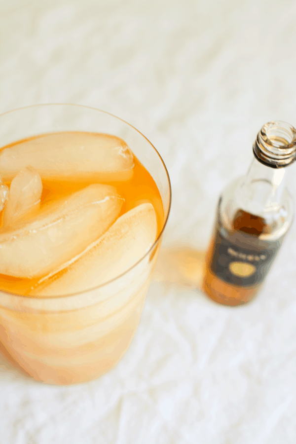 A close up of a glass with a cocktail juice cocktail made with rum with a mini bottle of rum on the table next to it.