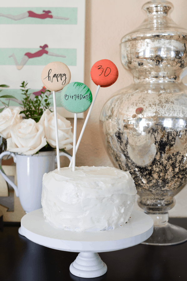 A cake with macrons on candy sticks written on with edible ink. 