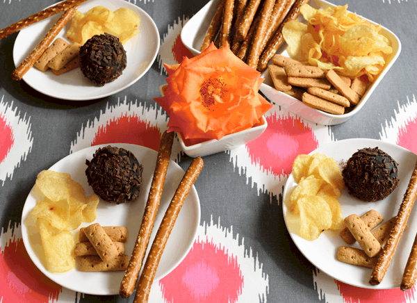 Small plates, each with an Oreo cookie ball, potato chips, pretzel rods and graham sticks on a table. 