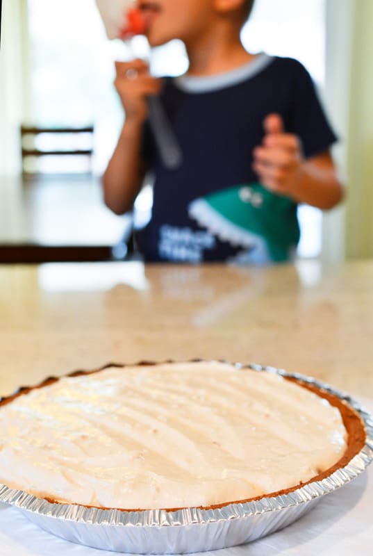 Frozen peanut butter pie on the counter with a child licking the spatula in the background.