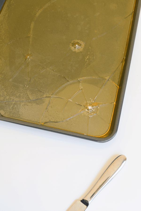 A knife and a sheet of hard candy that has started to be cracked on a plain white background.