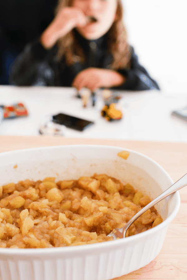 Baking dish with cooked applesauce with a kid and Legos in the background. 