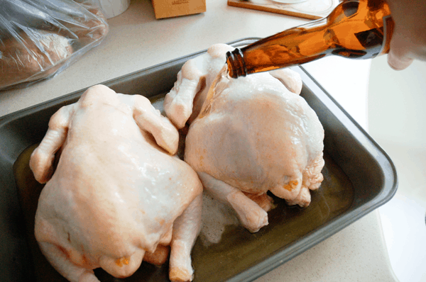 Pouring beer on raw chickens in a roasting pan.