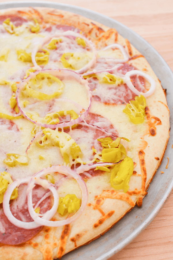 Close up of a pepperoncini pizza with red onion and salami on a pizza pan.