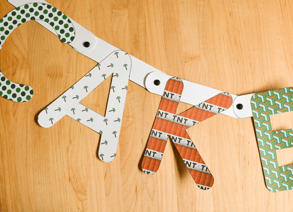 Close up of letters cut out of Minecraft paper that are strung together with brads to say cake for a party.