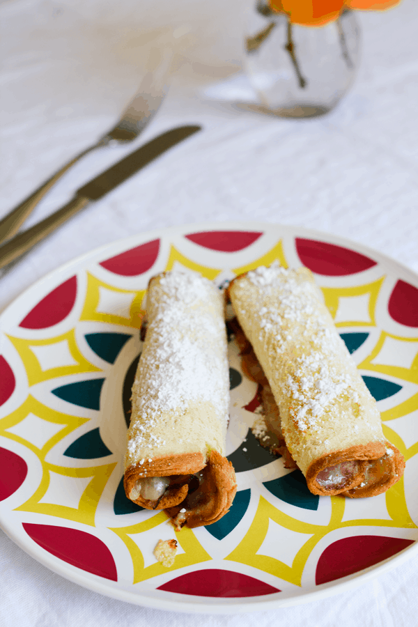 A close up of two pieces of Hawaiian Bread rolled up with melted cheese and ham inside and topped with powdered sugar. 