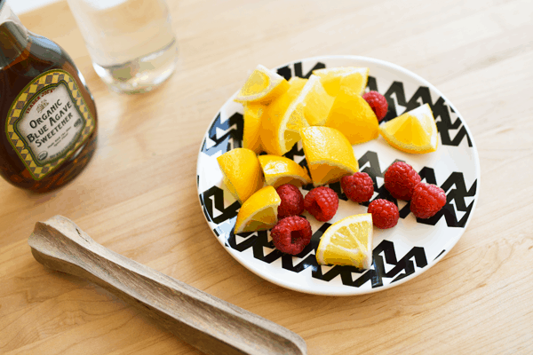 Meyer lemon slices and raspberries on a black and white plate.