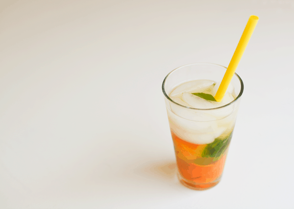 A glass of fruit infused water with ice and a yellow straw.