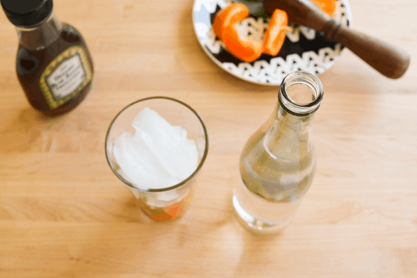 A cup with tangerine and basil topped with ice on a counter next to a bottle of water.