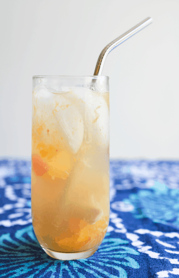 A glass filled with a delicious champagne cocktail with fresh ginger and peach on top of a blue table top. 