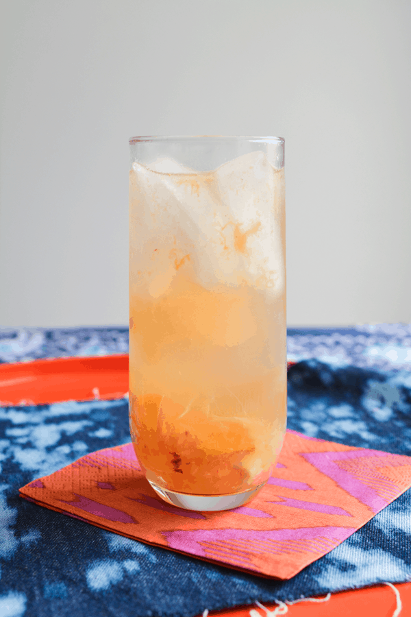 Sparkling wine cocktail with Sauvignon Blanc and fresh ginger and peaches in a tall cocktail glass on top of a brightly colored napkin.