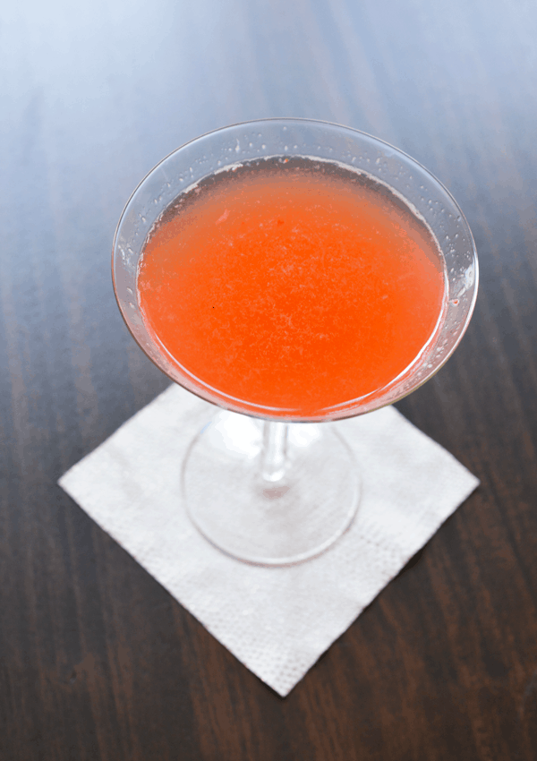 A strawberry sauvignon blanc cocktail with vodka in a martini glass on a table. 