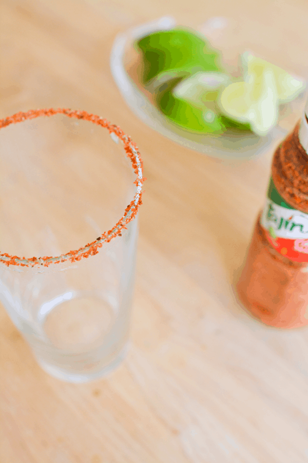 Empty glass with a Tajin rim with a bottle of Tajin next to it. 