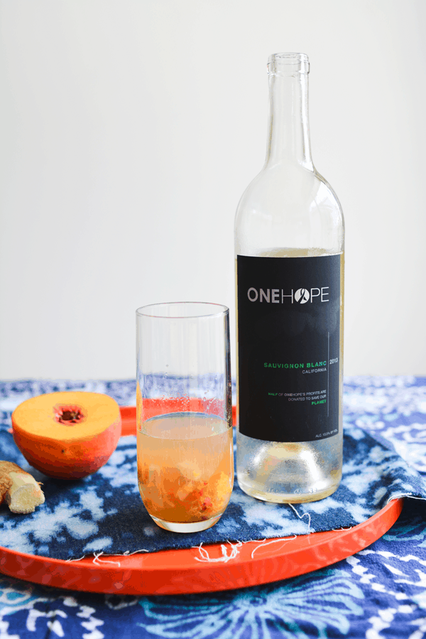 A red tray holding a bottle of sauvignon blanc, fresh peach and ginger, and a glass filled with ginger, peaches and sauvignon blanc.