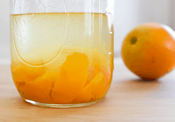 Orange peels infusing vodka in a mason jar with an orange next to it.