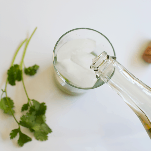 Topping a gin cocktail with sparkling wine and cilantro on a white tray.