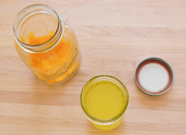 Orange infused vodka in a jar next to a lid with a larger jar and orange peels sitting next to it. 