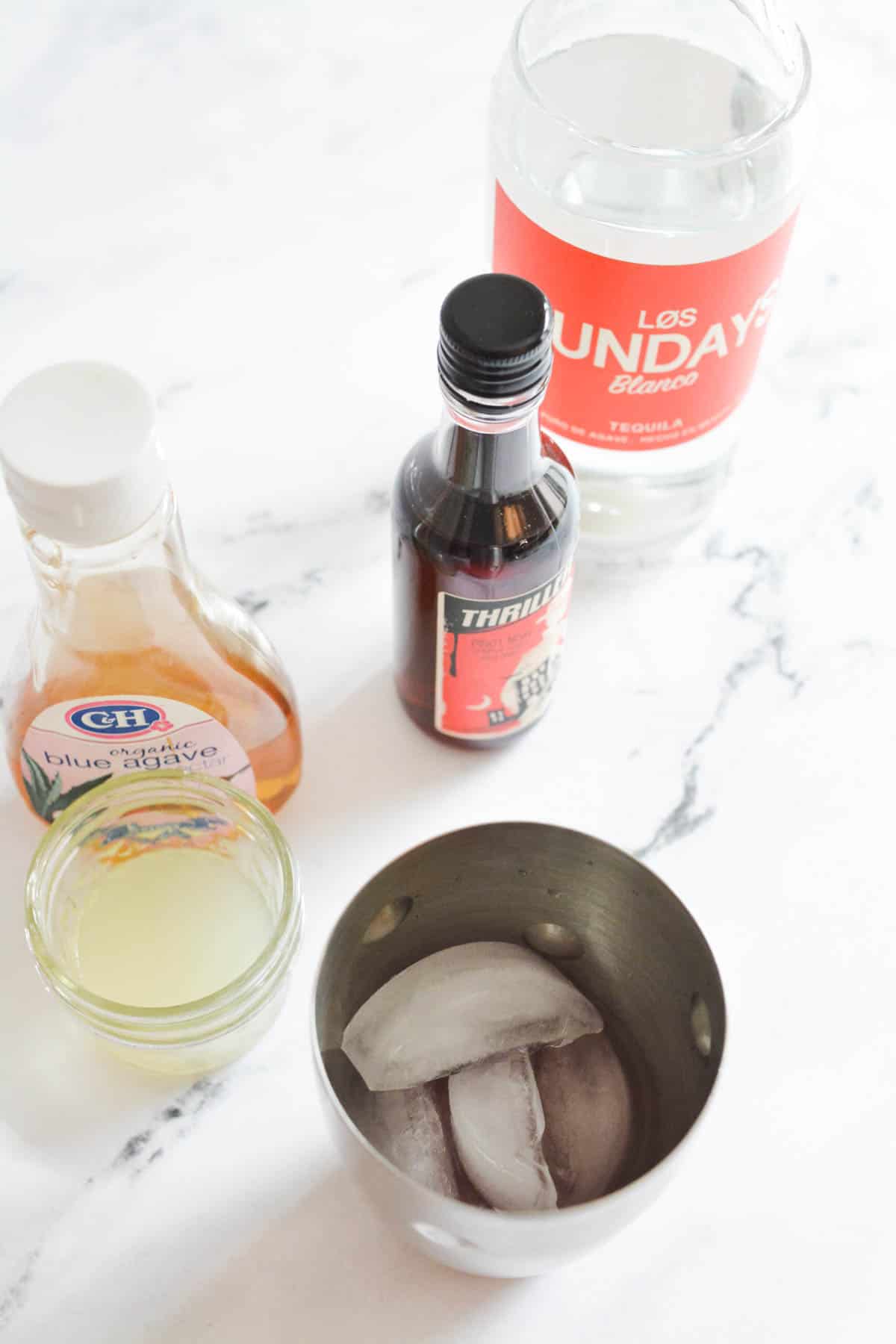 An overhead view of a counter with a cocktail shaker next to lime juice and other ingredients to make a drink.