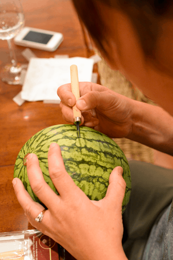 A woman carving a message into a watermelon. 