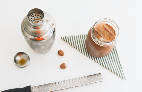 A cocktail shaker on a table next to a jar with iced coffee.