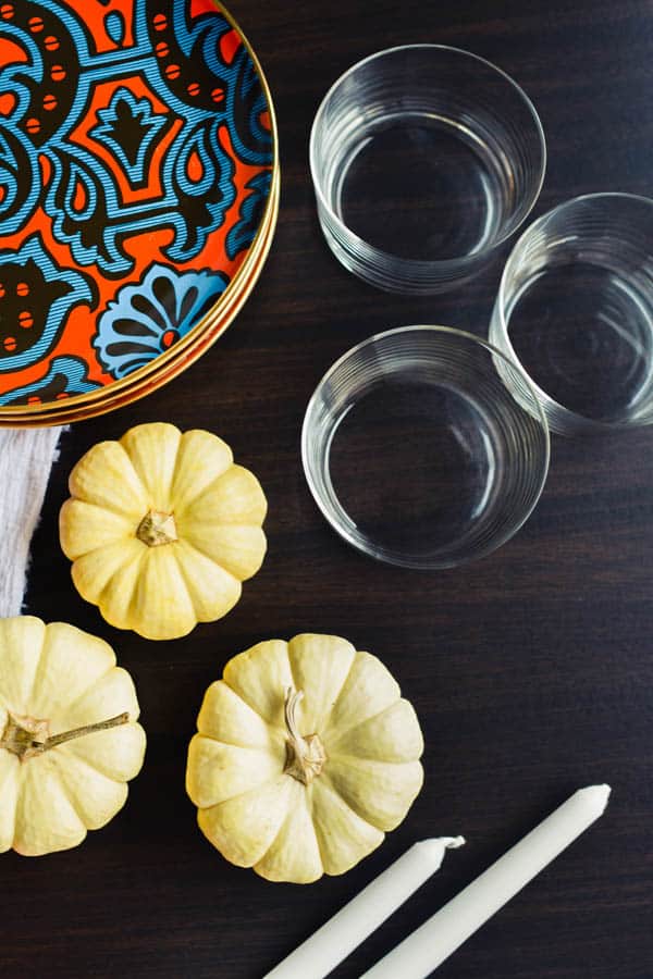 Top down view of plates, glasses and Thanksgiving decor to set a table for Friendsgiving.