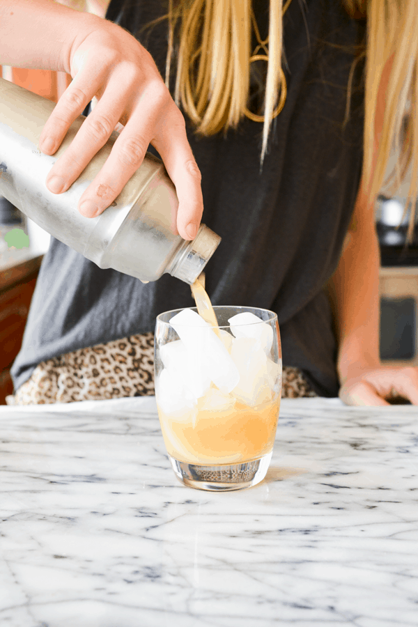 Woman pouring a cocktail from a shaker into a glass full of ice. 