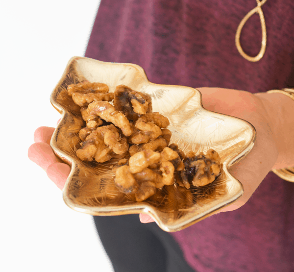 Girl holding a gold dish shaped like a Christmas tree full of candied walnuts.