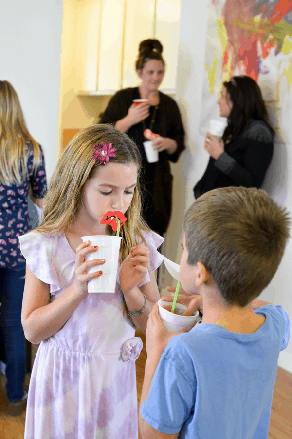 Two children enjoying ice cream floats in white plastic cups with silly straws.