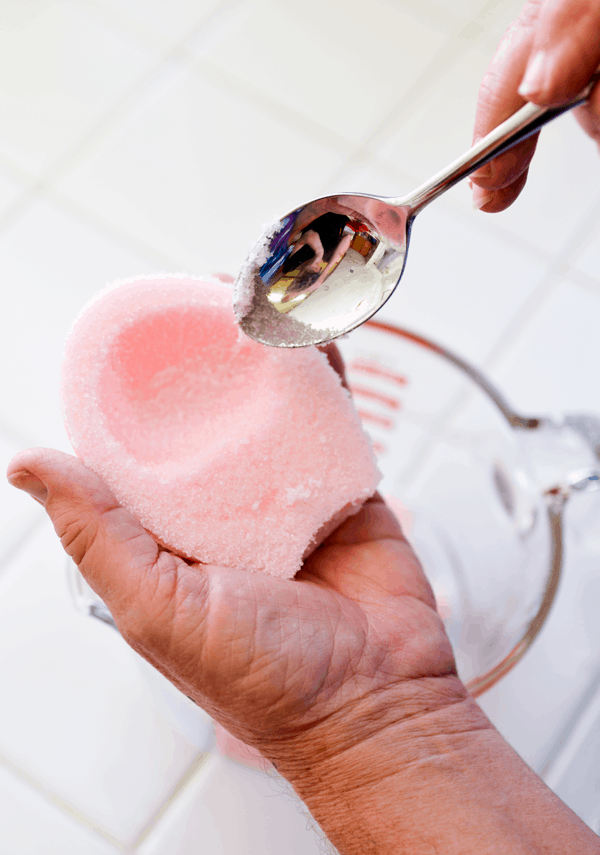 A pink sugar Easter egg being scraped with a spoon.