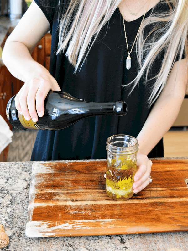 Woman adding prosecco to a jar to make champagne vinaigrette.