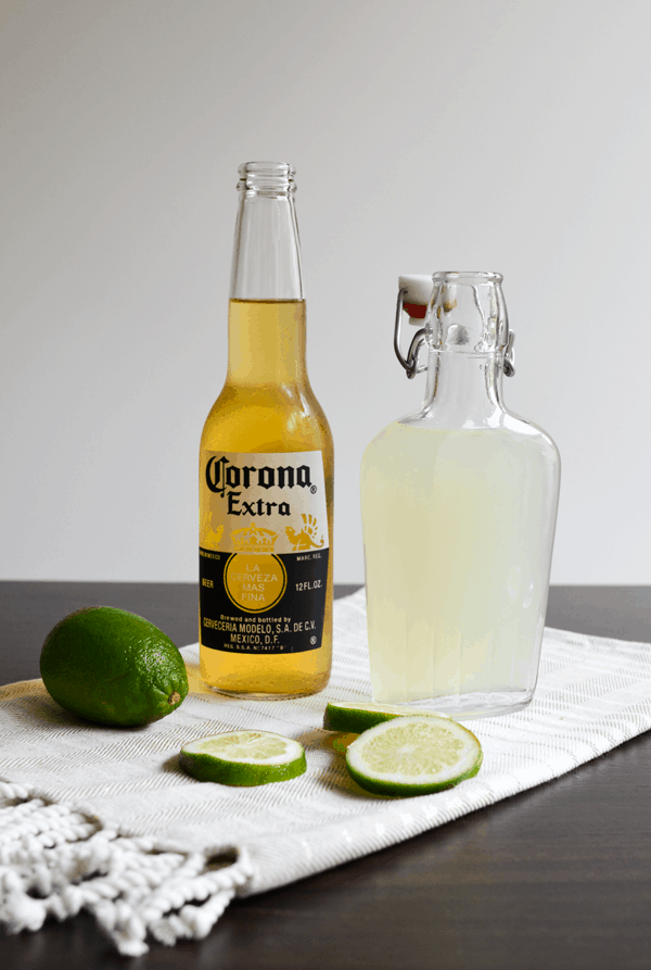 The ingredients to make a chelada - beer and limeade next to fresh lime slices.