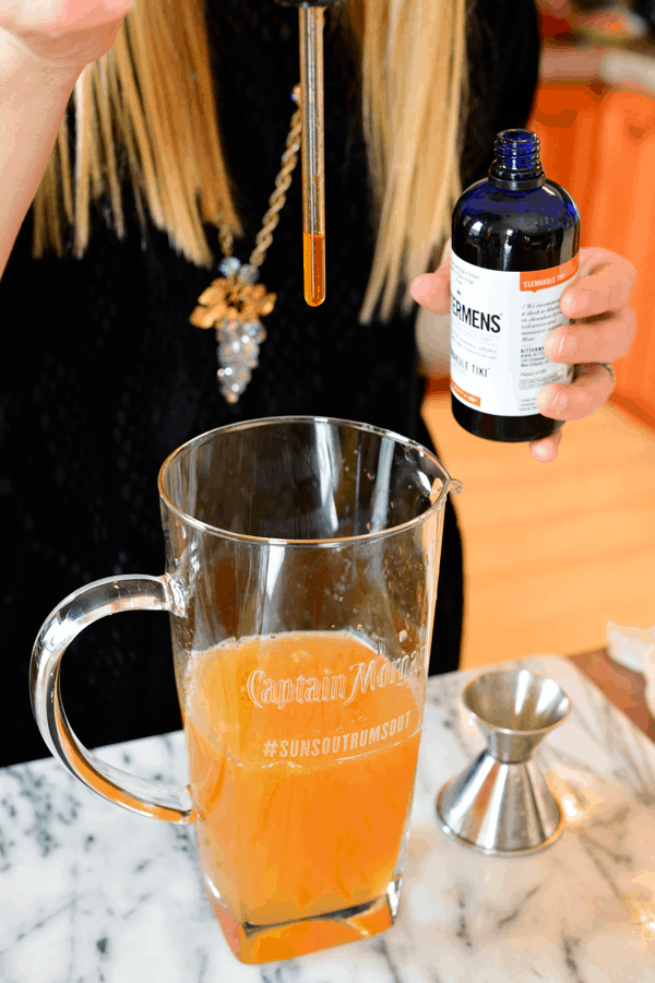 Woman adding bitters to a rum punch recipe for a party.