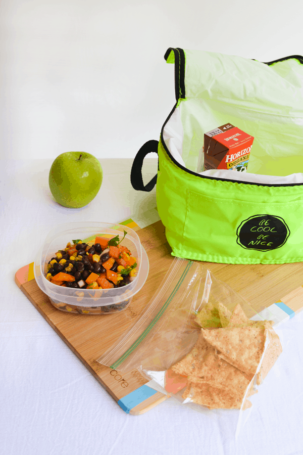 Plastic food storage container with black bean salad on a table next to a lunch pail.