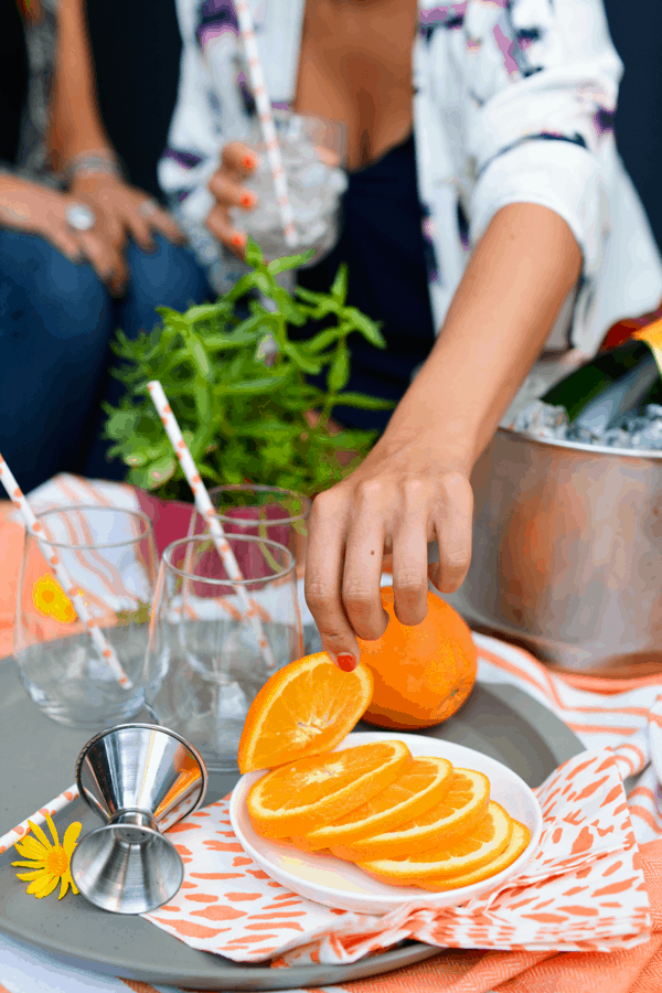 Girl reaching for a slice of orange to garnish her Aperol Spritz. 