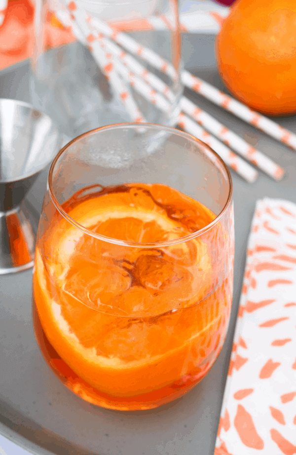 Aperol Spritz cocktail recipe in a stemless wine glass on a table. 