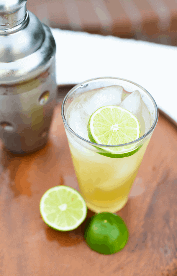 Spicy Serrano Margarita garnished with lime and ice on a wooden board next to a silver cocktail shaker.