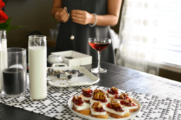 An adult Halloween party with appetizers on a plate on the table with a glass of wine and woman making a bracelet in the background.