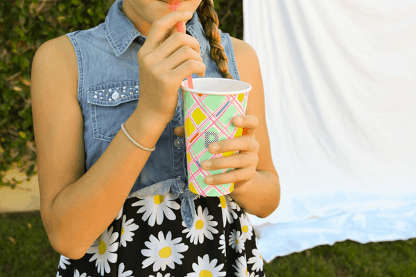 Girl drinking from a straw out of a colorful cup. 