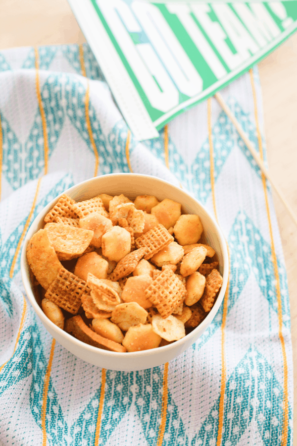 A small bowl of homemade Chex Mix on a decorative napkin next to a football pennant banner. 