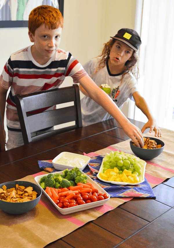 Two kids reaching for snacks on a table for a homegating party.